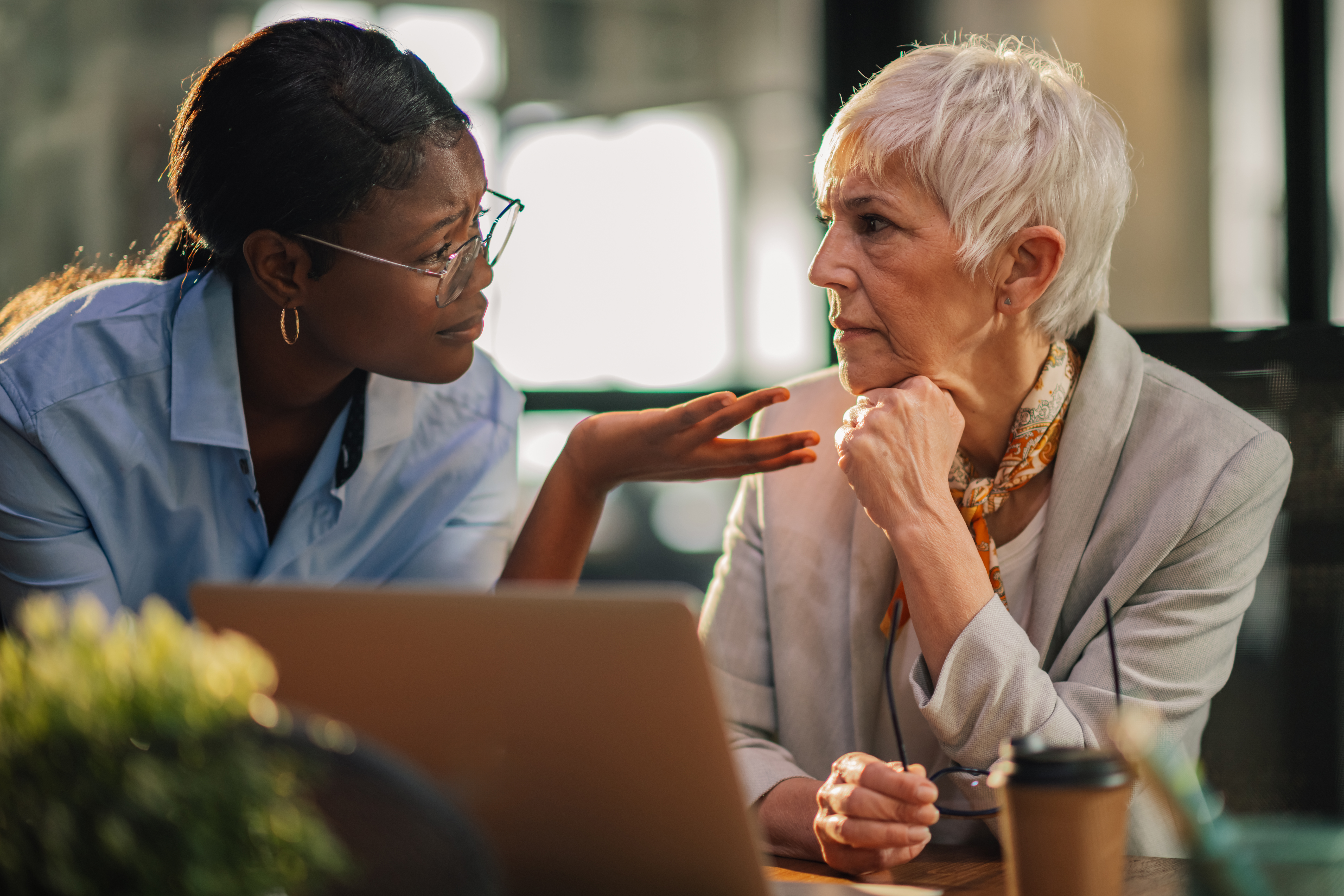 African american office worker explaining and discussing business strategy with her mature female mentor at modern workspace. Multicultural business women having consultations about startup project.